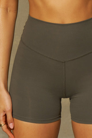 Close up detail front view of model from the waist down posing the soft and stretchy high-waisted sueded carob 2.5 inch Body Short with a wide waistband and shortened 2.5 inch inseam