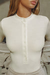 Close up front view of model posing in the fitted and stretchy bone rib Button Down Henley long sleeve top with a high crew neckline and front buttons that reach about halfway down the shirt