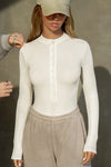 Front view of model posing in the fitted and stretchy bone rib Button Down Henley long sleeve top with a high crew neckline and front buttons that reach about halfway down the shirt