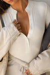 Close up detail front view of model posing in the fitted and stretchy bone rib Button Down Henley long sleeve top with a high crew neckline and front buttons that reach about halfway down the shirt