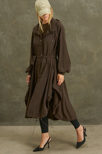 Full body front view of model posing in the espresso nylon City Trench coat with oversized silhouette, structured collar, attached hood, self-tie belt and adjustable sweep