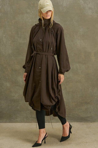 Full body front view of model posing in the espresso nylon City Trench coat with oversized silhouette, structured collar, attached hood, self-tie belt and adjustable sweep