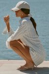 Side view of model posing outside by a lake in the lightweight natural white and blue stripe gauze Classic Button Down collared long sleeve shirt with front button closures