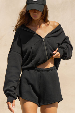 Front view of model posing in the relaxed fit black french terry Classic Sweat Short with side pockets, hidden drawstring, adjustable elastic waistband and JOAH BROWN logo patch on the bottom left leg