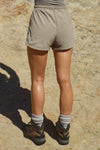 Back view of model from the waist down posing outside in the relaxed-fit desert sage nylon Classic Track Short with an elastic waistband, side seam pockets, and adjustable drawcord.