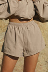 Close up front view of model from the waist down posing outside in the relaxed-fit fawn nylon Classic Track Short with an elastic waistband, side seam pockets, and adjustable drawcord.