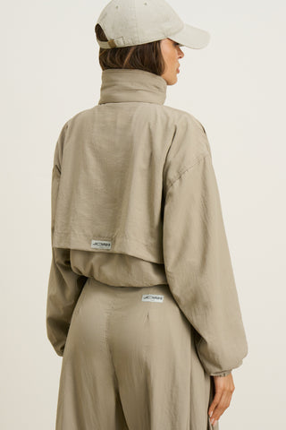 Back view of model posing in the relaxed-fit desert sage nylon Classic Windbreaker Jacket with a padded collared neck for structure & adjustable corded details at the sweep for cinching