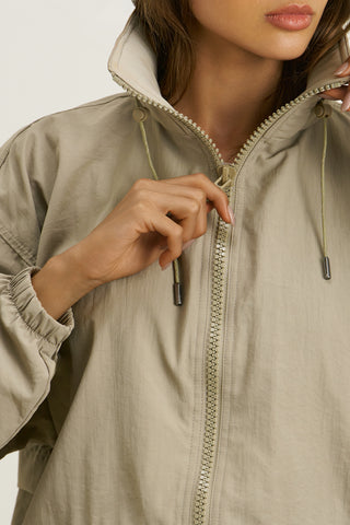 Close up detail front view of model posing in the relaxed-fit desert sage nylon Classic Windbreaker Jacket with a padded collared neck for structure & adjustable corded details at the sweep for cinching