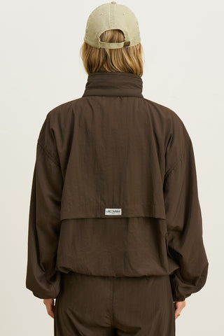 Back view of model posing in the relaxed-fit espresso-nylon Classic Windbreaker Jacket with a padded collared neck for structure & adjustable corded details at the sweep for cinching