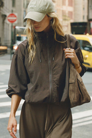 Front view of model posing in a city  in the relaxed-fit espresso nylon Classic Windbreaker Jacket with a padded collared neck for structure & adjustable corded details at the sweep for cinching