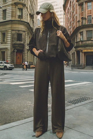 Full body front view of model posing in a city  in the relaxed-fit espresso nylon Classic Windbreaker Jacket with a padded collared neck for structure & adjustable corded details at the sweep for cinching