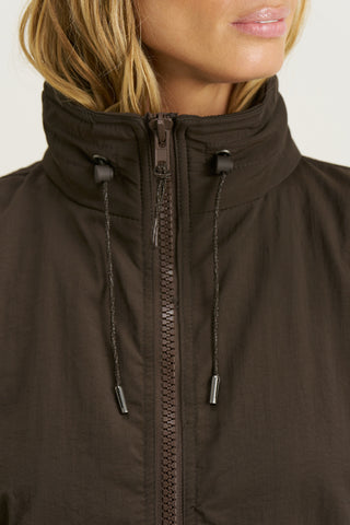 Close up detail front view of model posing in the relaxed-fit espresso nylon Classic Windbreaker Jacket with a padded collared neck for structure & adjustable corded details at the sweep for cinching