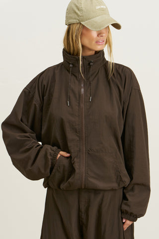 Front view of model posing in the relaxed-fit espresso nylon Classic Windbreaker Jacket with a padded collared neck for structure & adjustable corded details at the sweep for cinching