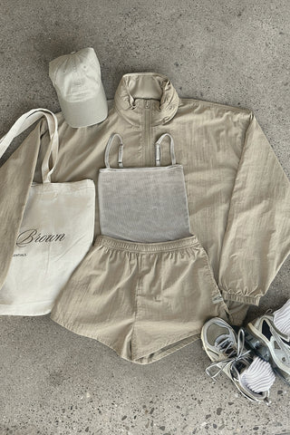 Flat lay view of the dune washed rib Square Neck Cami, desert sage nylon Classic Windbreaker Jacket, desert sage nylon Classic Track Short, sahara Official Cap and salt Scrunch Sock