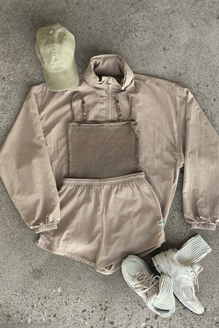 Flat lay view of the sepia washed rib Square Neck Cami, fawn nylon Classic Windbreaker Jacket, fawn nylon Classic Track Short, desert Official Cap and off white Scrunch Sock