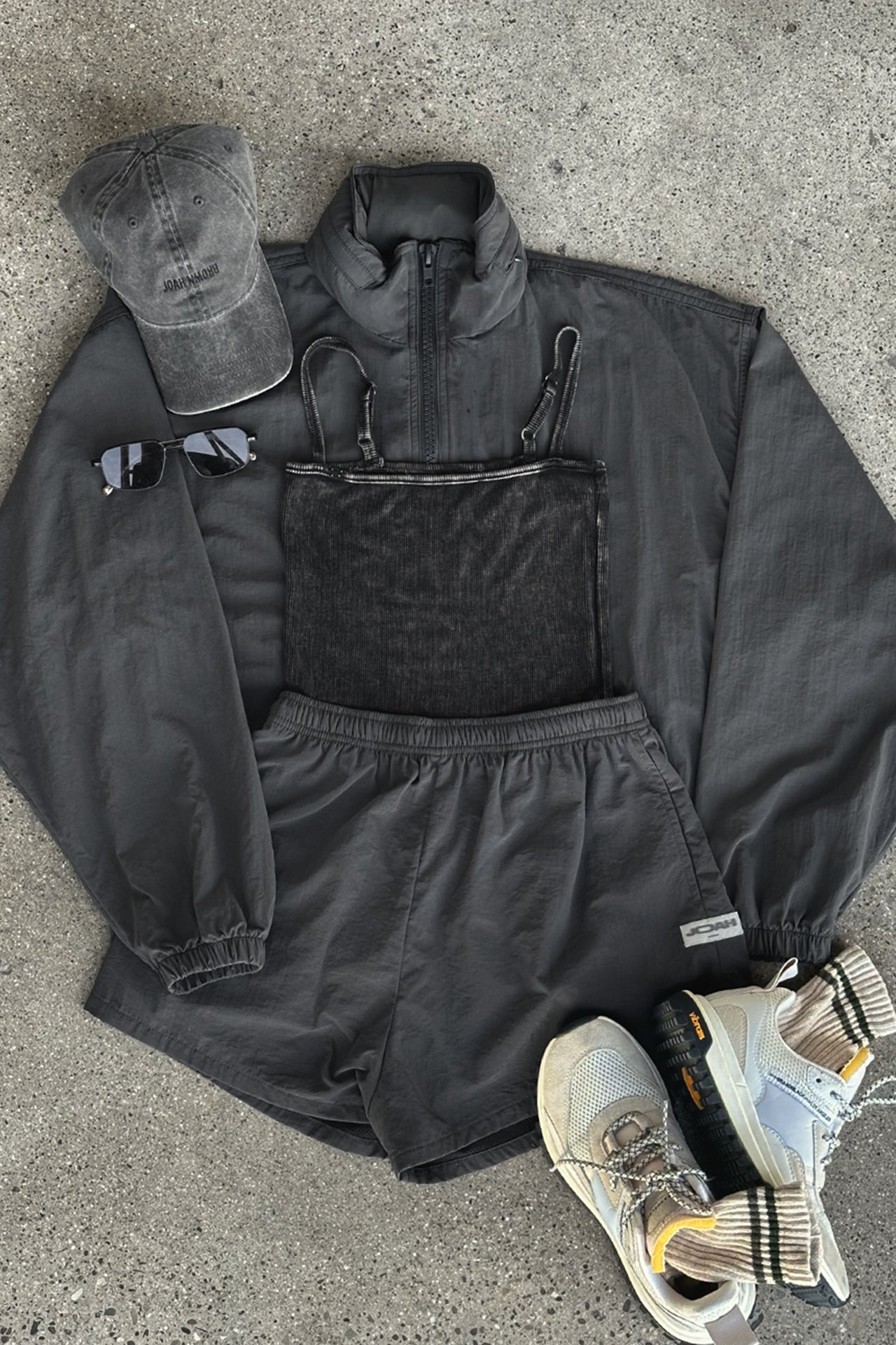 Flat lay view of the charcoal washed rib Square Neck Cami, jet nylon Classic Windbreaker Jacket, jet nylon Classic Track Short, washed black Official Cap and oat and olive Hiker Sock
