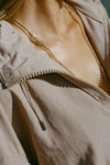 Close up detail view of the front of the oversized fawn nylon Classic Windbreaker Jacket with a collar, zip-away hood and reflective corded details at the hem, sleeves and neck for cinching.