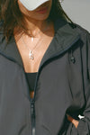 Close up detail front view of model posing in the oversized jet nylon Classic Windbreaker Jacket with a collar, zip-away hood and reflective corded details at the hem, sleeves and neck for cinching.