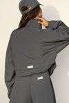 Back view of model posing in the oversized jet nylon Classic Windbreaker Jacket with a collar, zip-away hood and reflective corded details at the hem, sleeves and neck for cinching.