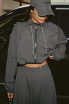 Front view of model posing in the oversized jet nylon Classic Windbreaker Jacket with a collar, zip-away hood and reflective corded details at the hem, sleeves and neck for cinching.