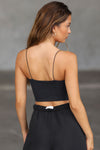 Back view of model posing in the fitted cropped sueded onyx Contour Corset tank top with delicate corded straps, a curved hem and paneling on the bodice