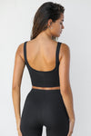 Back view of model posing in the cropped stretchy sueded onyx Contour Crop Tank with a scoop back