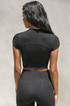Back view of model posing in the fitted cropped black rib Contrast Stitch Crop Tee with stitched seaming, cap sleeves and a mini mock neckline
