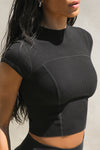 Close up detail side view of model posing in the fitted cropped black rib Contrast Stitch Crop Tee with stitched seaming, cap sleeves and a mini mock neckline