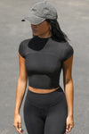 Front view of model posing in the fitted cropped black rib Contrast Stitch Crop Tee with stitched seaming, cap sleeves and a mini mock neckline