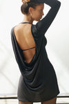 Back view model posing in the relaxed fit black modal Cowl Back Long Sleeve Mini Dress \with a crew neckline, A-line silhouette, adjustable straps at the center back and neck and an open back with a draped cowl detail.