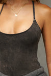 Close up detail front view of model posing in the fitted charcoal washed rib Cross Back Cami with a scoop neckline and thin adjustable straps that criss cross in the back