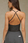 Back view of model posing in the fitted charcoal washed rib Cross Back Cami with a scoop neckline and thin adjustable straps that criss cross in the back