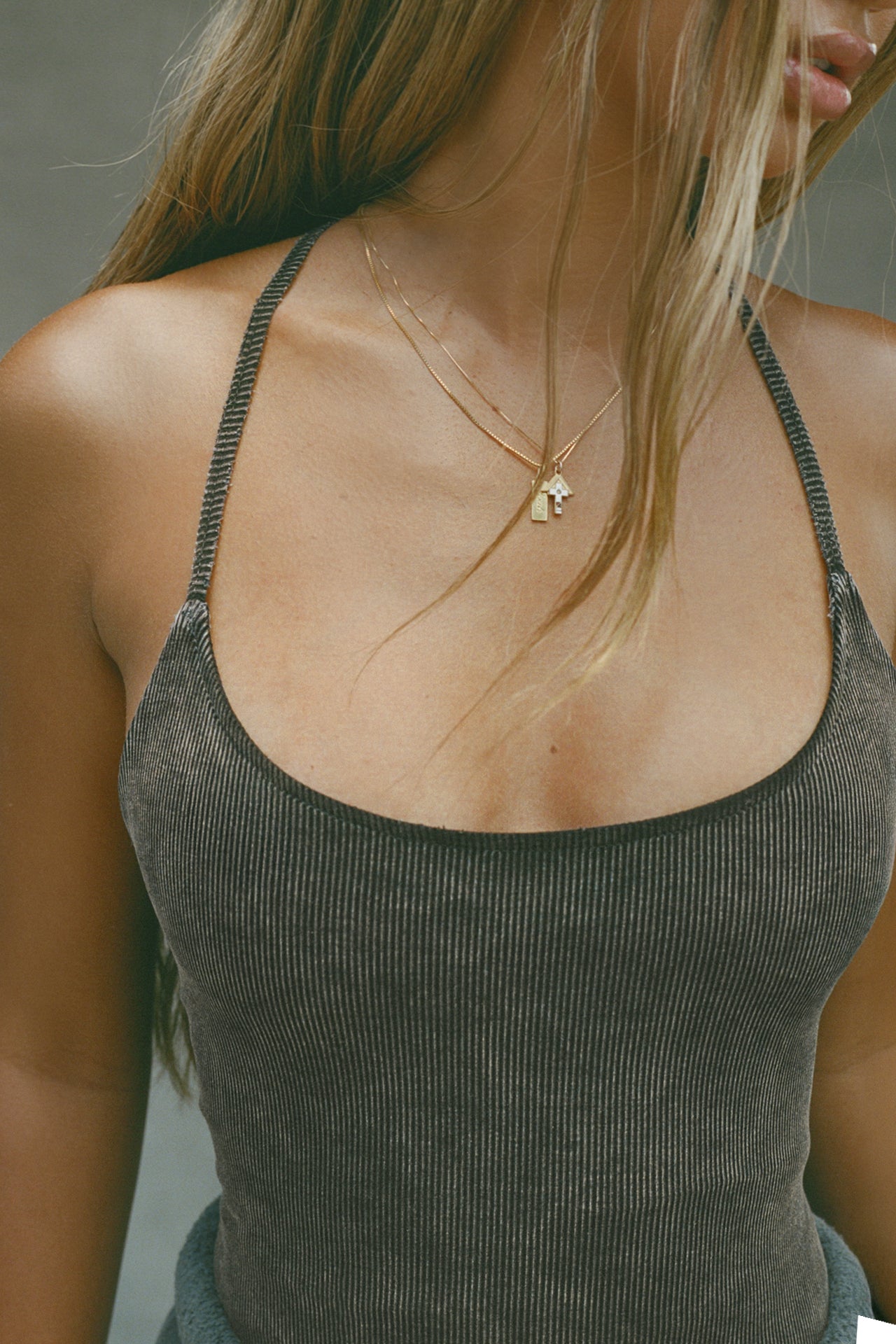 Close up detail front view of model posing in the fitted charcoal washed rib Cross Back Cami with a scoop neckline and thin adjustable straps that criss cross in the back