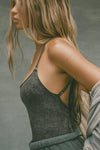 Close up side view of model posing in the fitted charcoal washed rib Cross Back Cami with a scoop neckline and thin adjustable straps that criss cross in the back