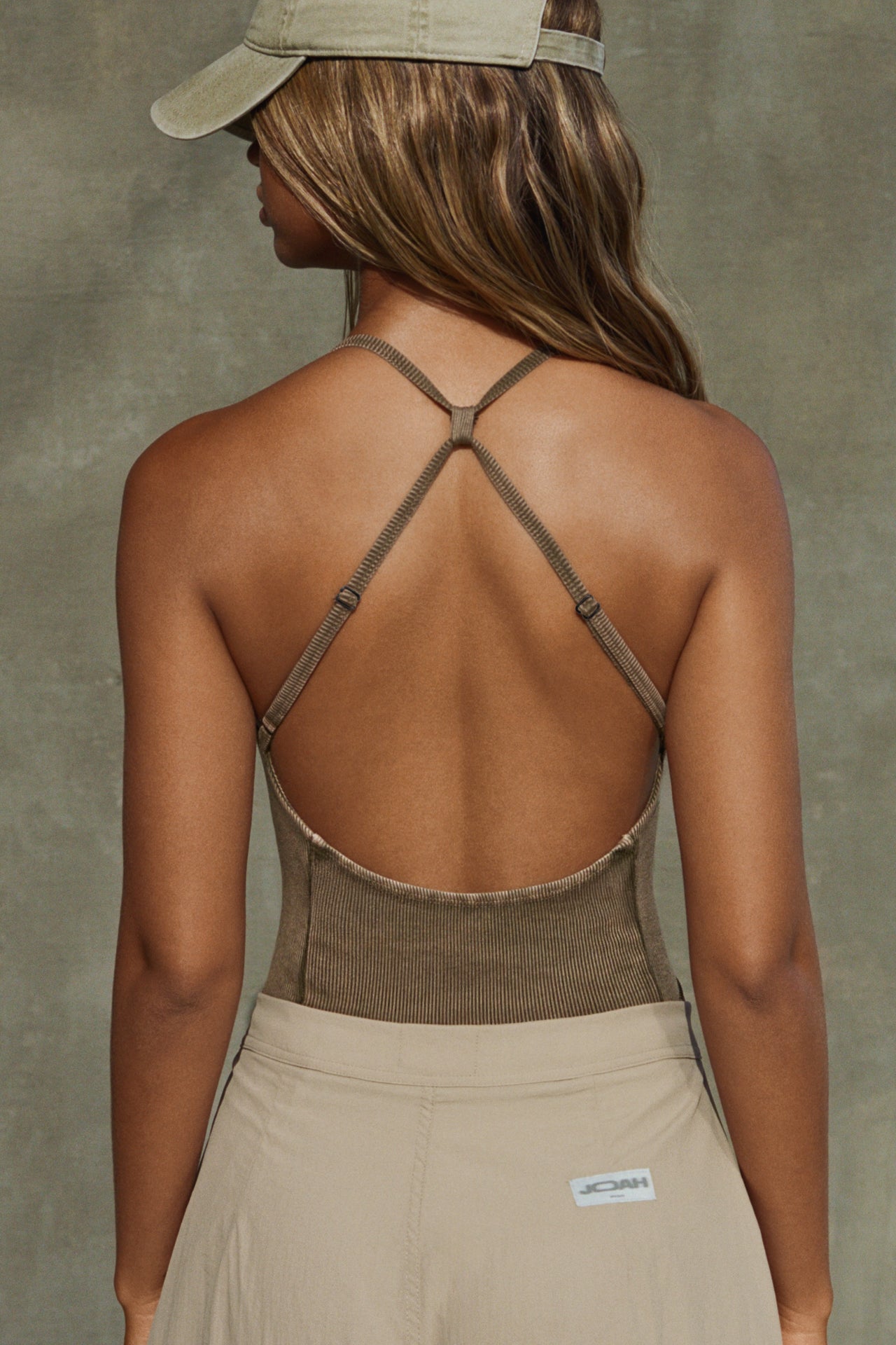 Back view of model posing in the fitted sepia washed rib Cross Back Cami with a scoop neckline and thin adjustable straps that criss cross in the back