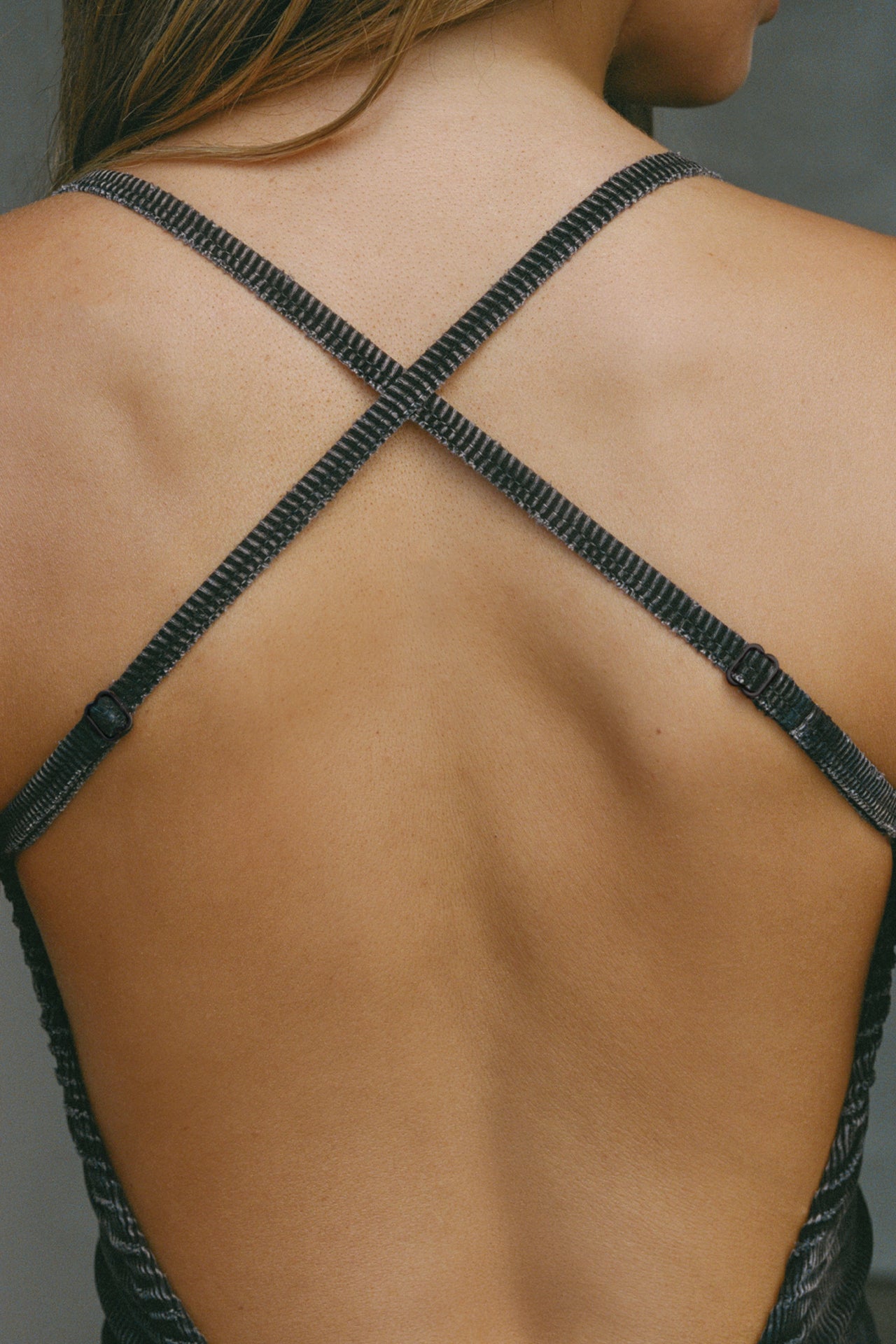 Close up detail back view of model posing in the fitted  charcoal washed rib Cross Back Midi Dress with an asymmetrical hem, a low scoop back and thin adjustable straps that criss cross in the back