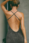 Back view of model posing in the fitted  charcoal washed rib Cross Back Midi Dress with an asymmetrical hem, a low scoop back and thin adjustable straps that criss cross in the back