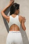 Back view of model posing in the fitted cropped bone flexrib Curve Crop Tank with a vertical stitch detail down the back, a curved hemline in an inverted u-shape and mini v back