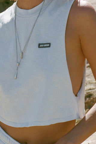 Close up detail front view of model posing outside by a truck in the relaxed fit cloud cotton Cut Off Boyfriend Tank with low cut armholes, a crew neckline and a joah brown logo patch at the upper left chest