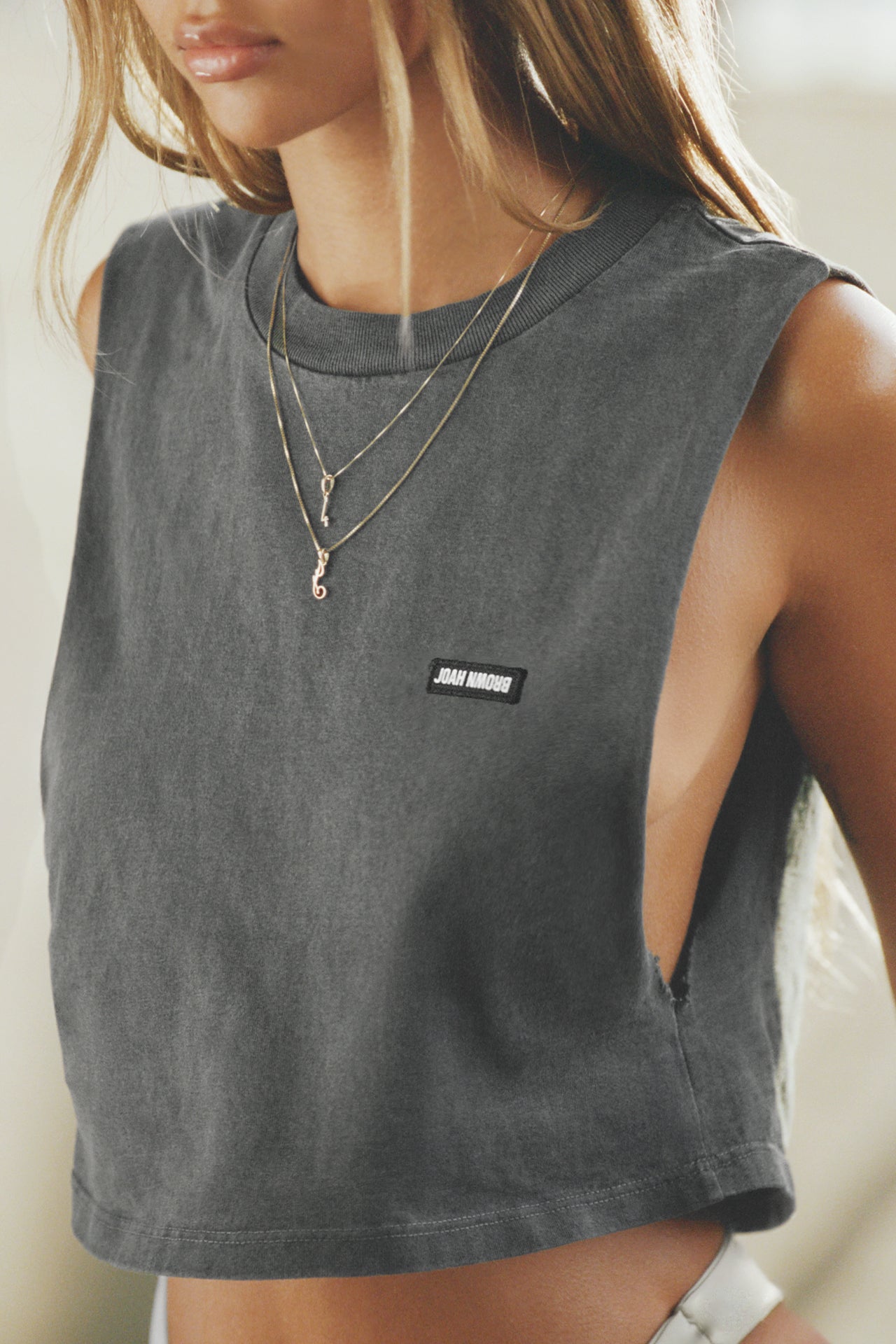 Close up front view of model posing in the relaxed fit washed black cotton Cut Off Boyfriend Tank with low cut armholes, a crew neckline and a joah brown logo patch at the upper left chest