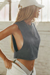 Side view of model posing in the relaxed fit washed black cotton Cut Off Boyfriend Tank with low cut armholes, a crew neckline and a joah brown logo patch at the upper left chest