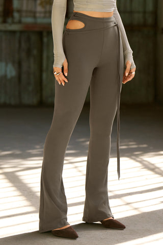 Side view of model from the waist down posing in the fitted, bootcut style sueded carob Cutout Mini Flare Legging with a side keyhole cutout and strappy, self-adjusting ties at the waist
