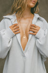 Close up front view of model posing in the oversized pearl grey luxe knit Deep V Pullover with a plunging collared neckline and dropped shoulders