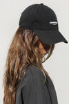 Side view of model wearing the six-panel black with bubble print Official Cap with a curved brim and an embroidered white Joah Brown bubble logo on the front