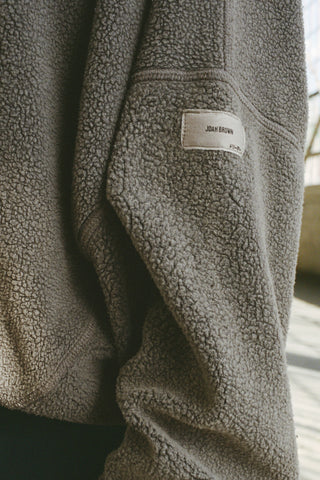 Close up detail front view of model posing in the relaxed fit oakmoss sherpa Drop Shoulder Pullover sweatshirt with an exaggerated crew neckline, dropped shoulders and a custom Joah Brown Logo Patch on the left sleeve 