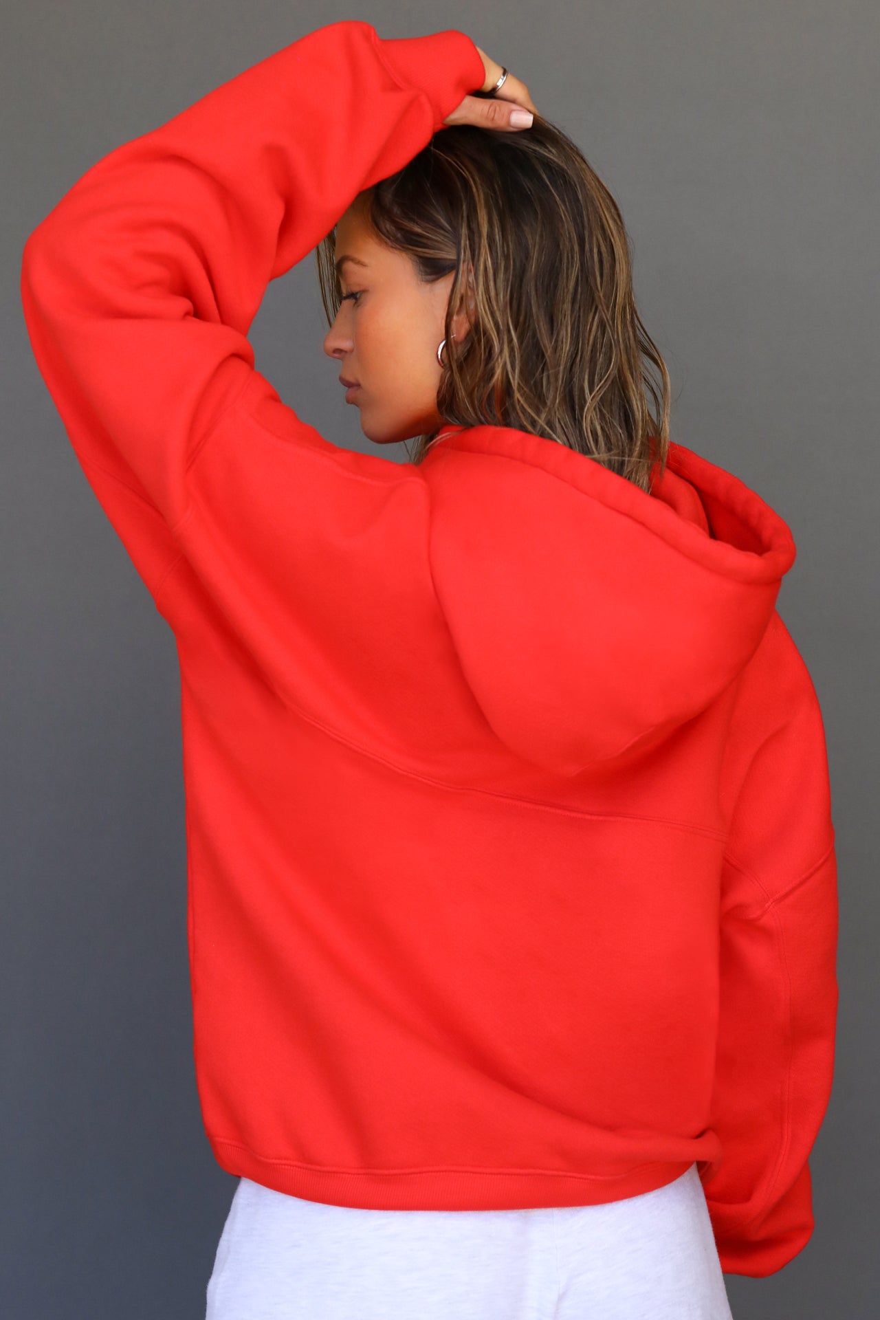 Back view of model posing in the oversized comfortable hot sauce french terry Oversized Pullover Hoodie sweatshirt with paneling on the back and arms and thumbholes