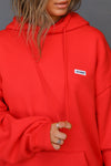 Close up detail front view of model posing in the oversized comfortable hot sauce french terry Oversized Pullover Hoodie sweatshirt with a Joah Brown logo patch at the front left chest, kangaroo pocket, drawstrings and thumbholes