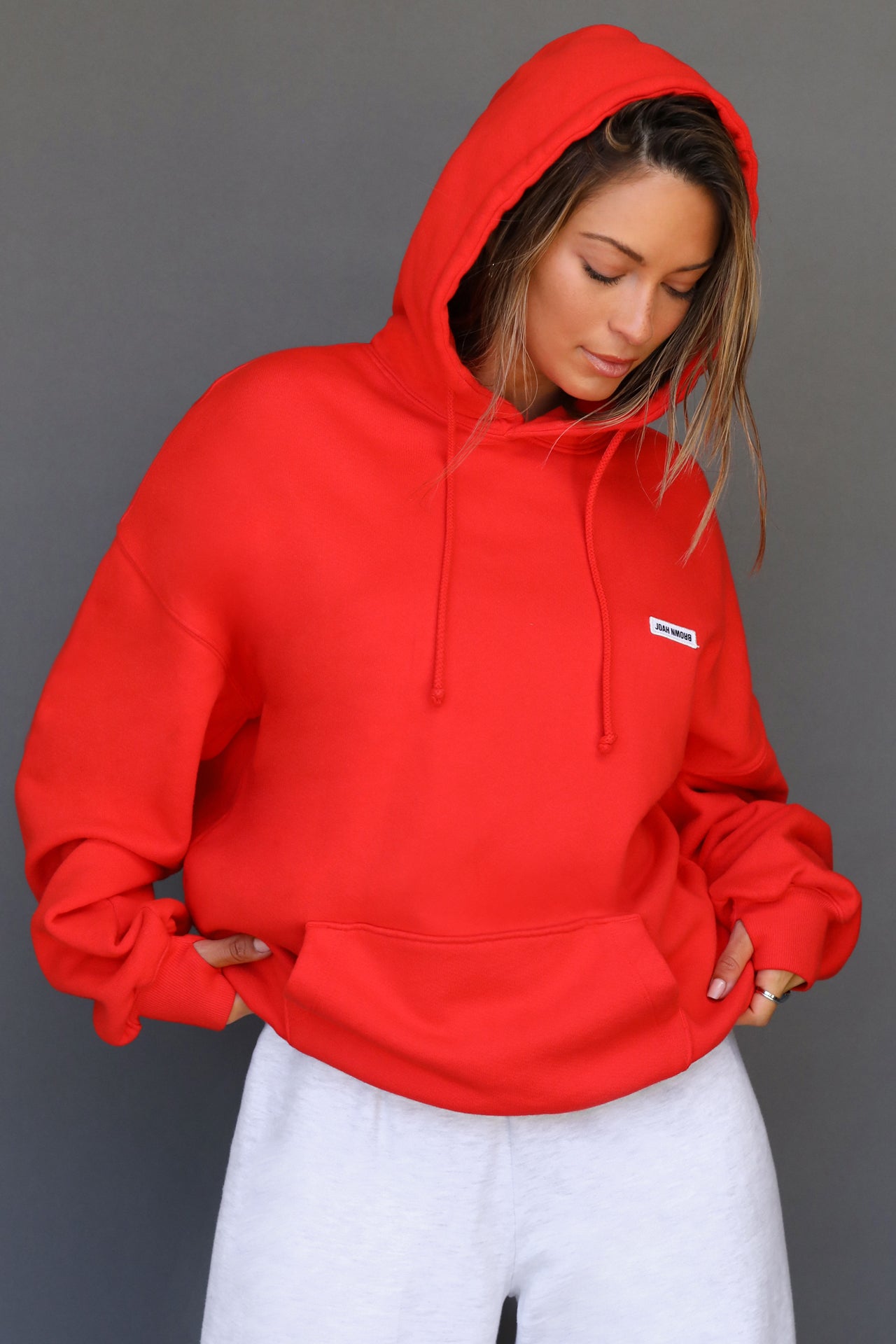 Front view of model posing in the oversized comfortable hot sauce french terry Oversized Pullover Hoodie sweatshirt with a Joah Brown logo patch at the front left chest, kangaroo pocket, drawstrings and thumbholes