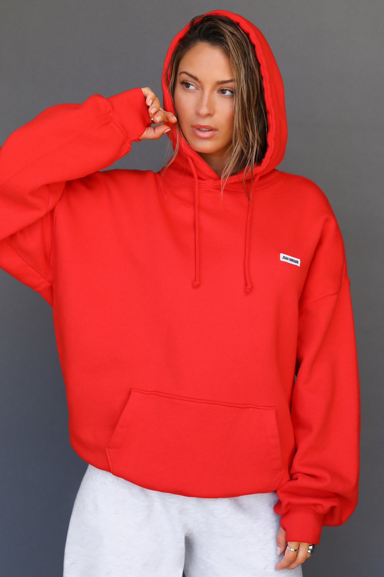 Front view of model posing in the oversized comfortable hot sauce french terry Oversized Pullover Hoodie sweatshirt with a Joah Brown logo patch at the front left chest, kangaroo pocket, drawstrings and thumbholes