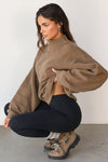 Side view of model crouching and posing in the comfortable cocoa french terry Turtleneck Sweatshirt pullover with a side split in the collar and a slightly oversized fit